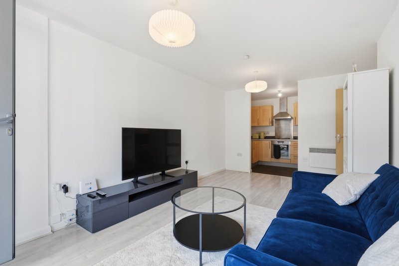 Modern living room with blue sofa, TV, round coffee table and kitchen area