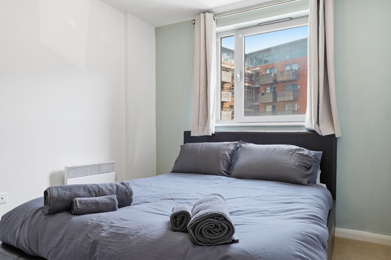 Compact bedroom with double bed, gray bedding, black headboard and window view of brick building