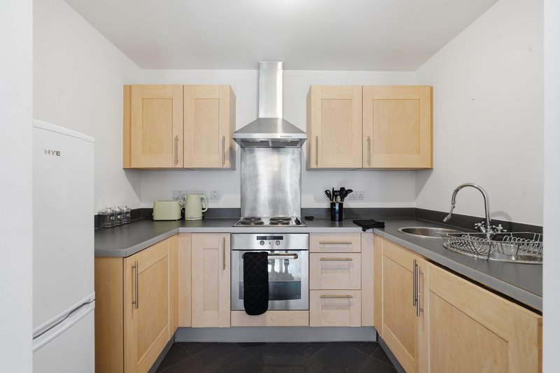Modern kitchen with light wood cabinets, black countertops, stainless steel appliances and splashback