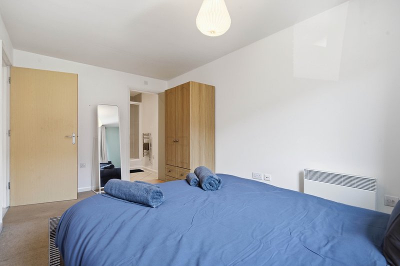 Bedroom with blue double bed, wooden wardrobe, light fixture and door to ensuite