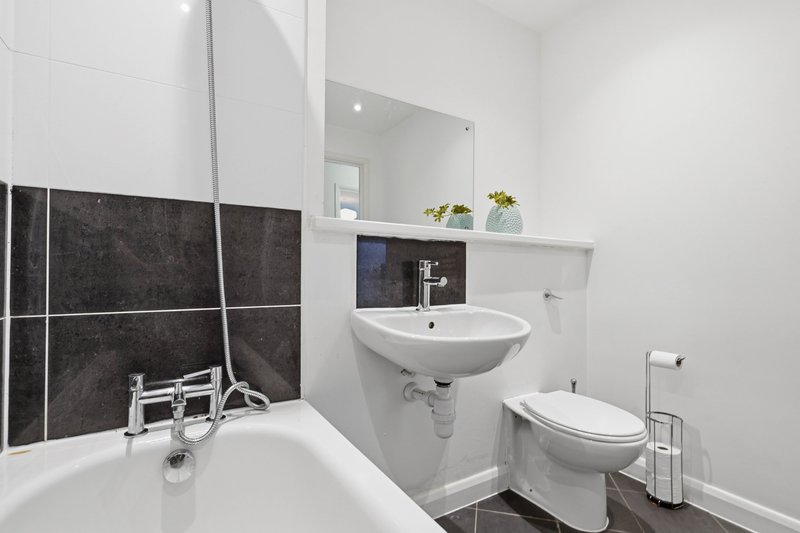 Modern bathroom with white sink, toilet, bathtub and dark tile feature wall