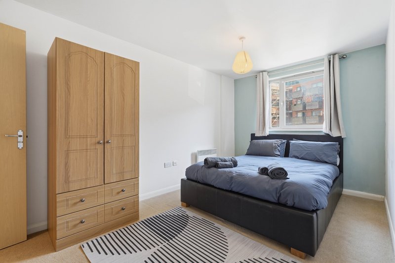 Bright bedroom with double bed, wooden wardrobe, striped rug and pendant light