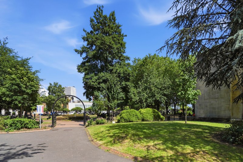 Modern residential building exterior with manicured grounds, trees and paved pathway