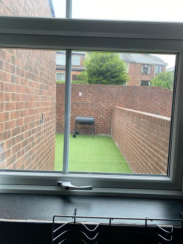 View through glass sliding door to small brick-walled courtyard with artificial grass