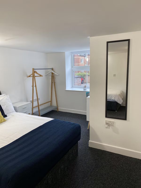 Bedroom with double bed, wooden clothes rack, mirror, and window with street view