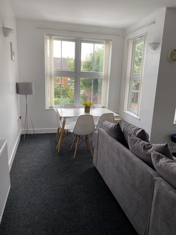 Bright sitting area with gray sofa, small white table, chairs, and large windows overlooking garden