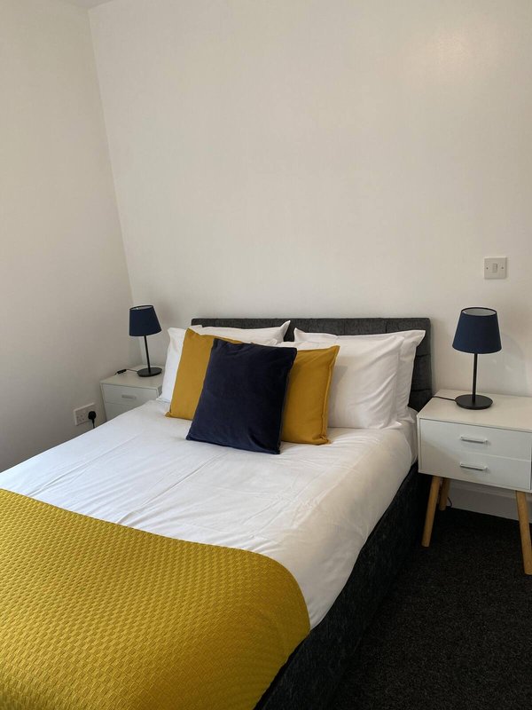 Modern bedroom with double bed, yellow throw, navy and gold cushions, bedside tables and lamps