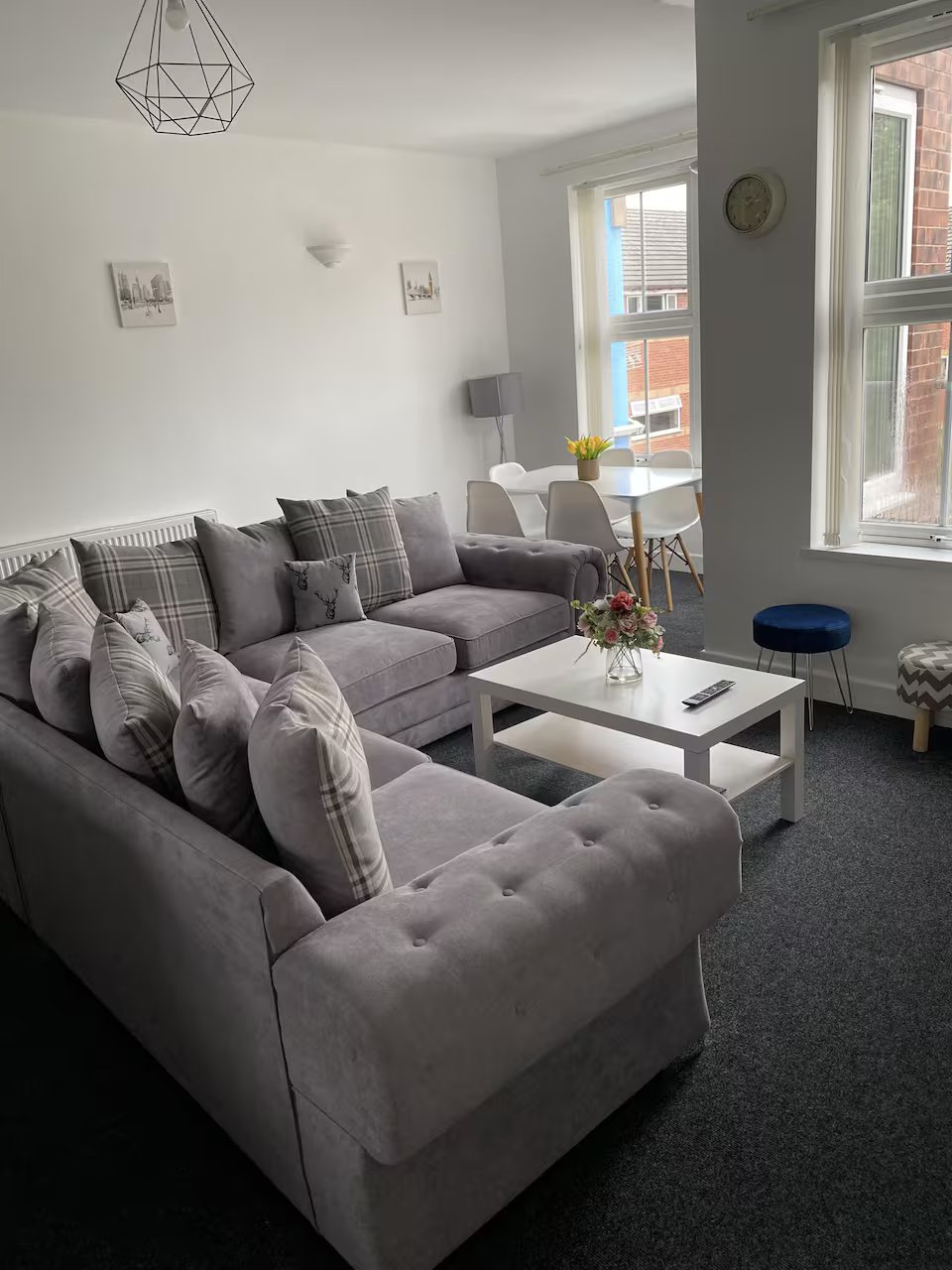 Modern living room with grey upholstered sofas, geometric pendant light, white coffee table and large windows.