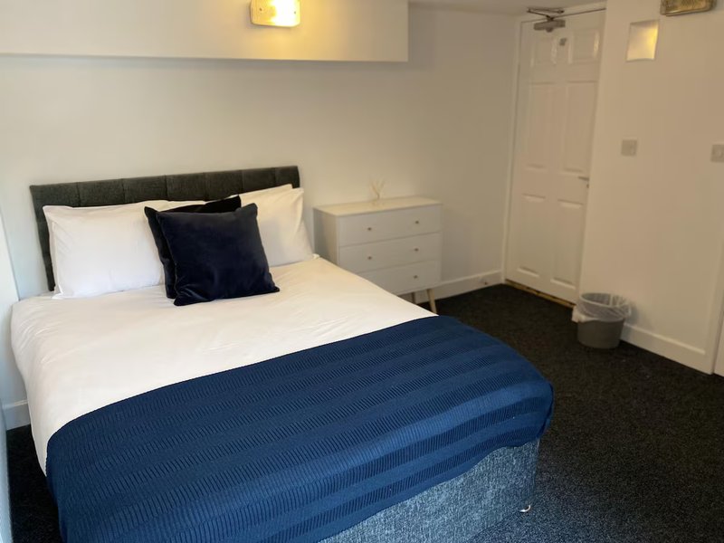 Bedroom with double bed, navy bedding, black headboard, white chest of drawers and door