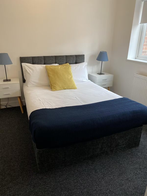 Bedroom with double bed, gray headboard, white bedding, yellow cushion, blue throw blanket