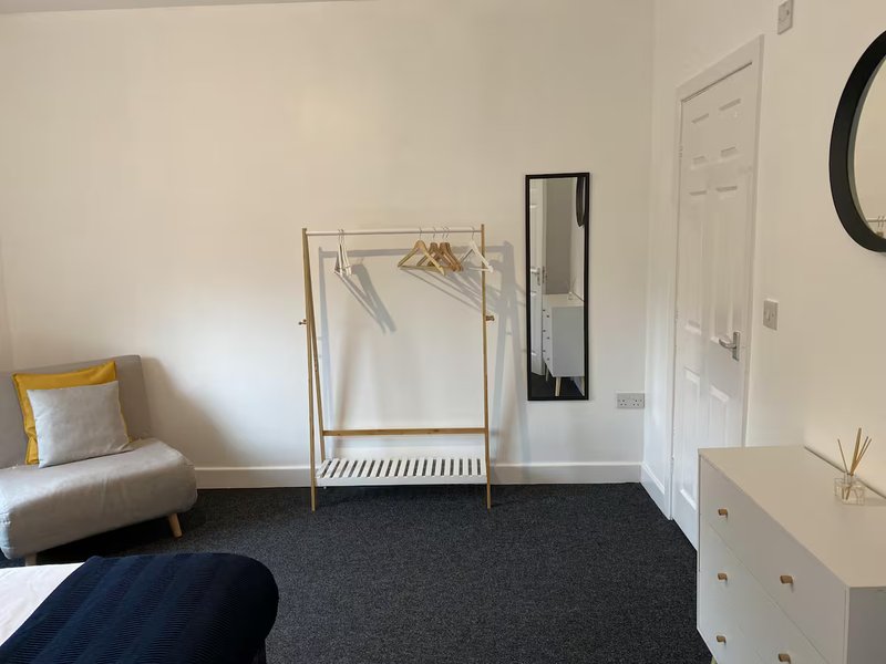 Bright bedroom with single bed, clothing rail, white wardrobe and round mirror