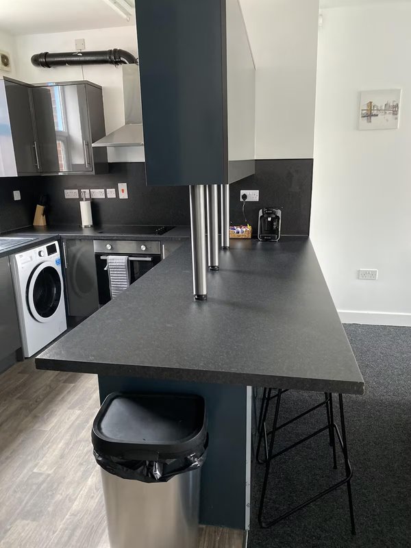 Modern kitchen with black countertop, island seating, washing machine and built-in appliances