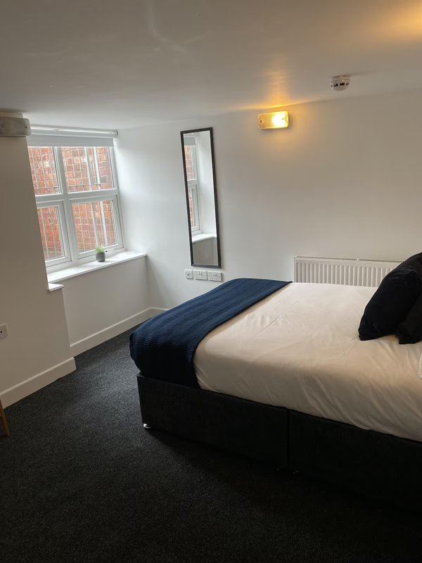 Bright bedroom with double bed, window, wall-mounted mirror, and radiator heater