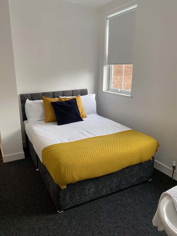 Bedroom with double bed, yellow bedding, white pillows, window with blind.