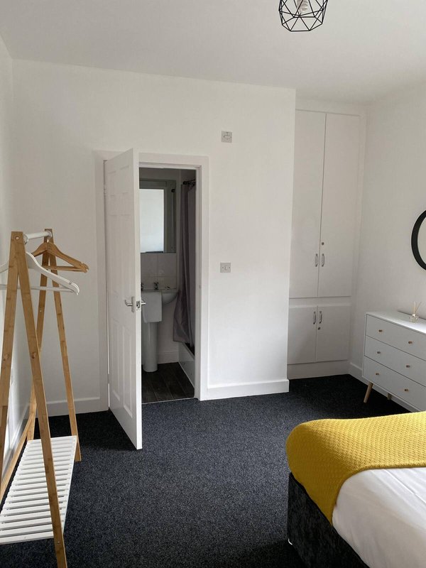 Bedroom with double bed, wooden coat stand, white wardrobe and dark carpet flooring