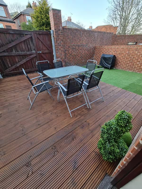 Outdoor patio with dining table, chairs, decking, brick walls and artificial turf