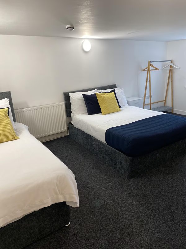 Twin bedroom with two beds, dark carpet, yellow and navy cushions, wooden clothes rail.