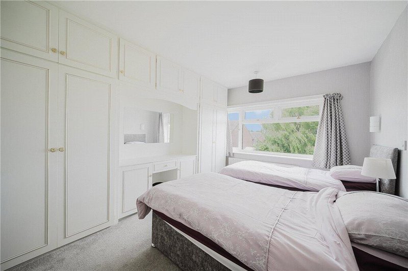 Bright bedroom with twin beds, built-in white wardrobes, dressing table and window view
