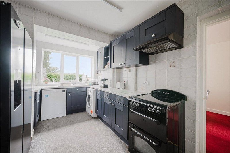 Modern kitchen with dark cabinets, black  range cooker, stainless steel fridge and window overlooking garden