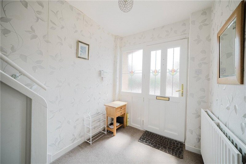 Bright hallway with marble-effect wallpaper, wooden stool, glass door and radiator