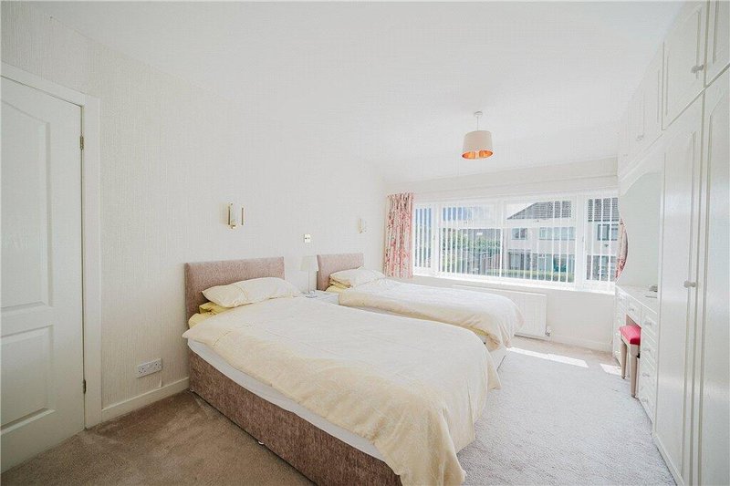 Bright bedroom with double bed, cream bedding, large window and neutral carpeting