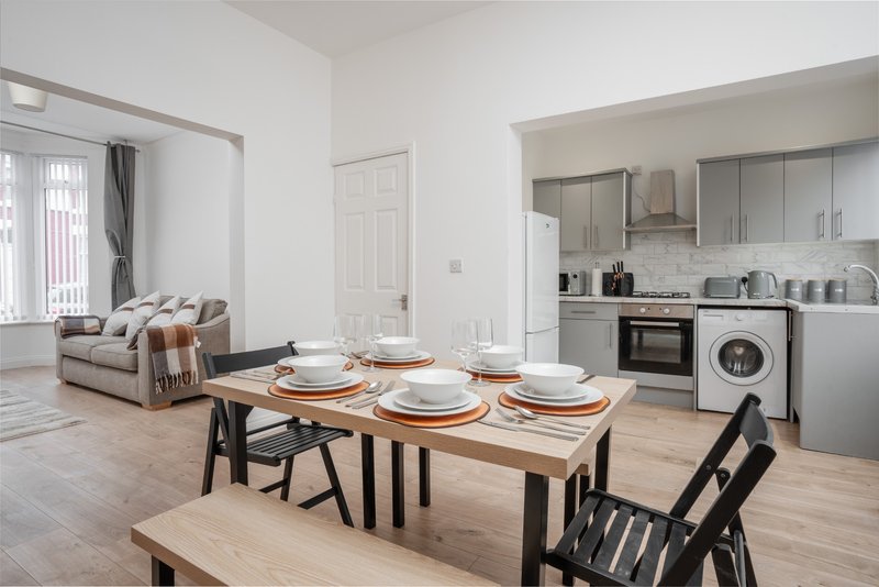 Open-plan living space with dining table, kitchen area, and sofa with throws