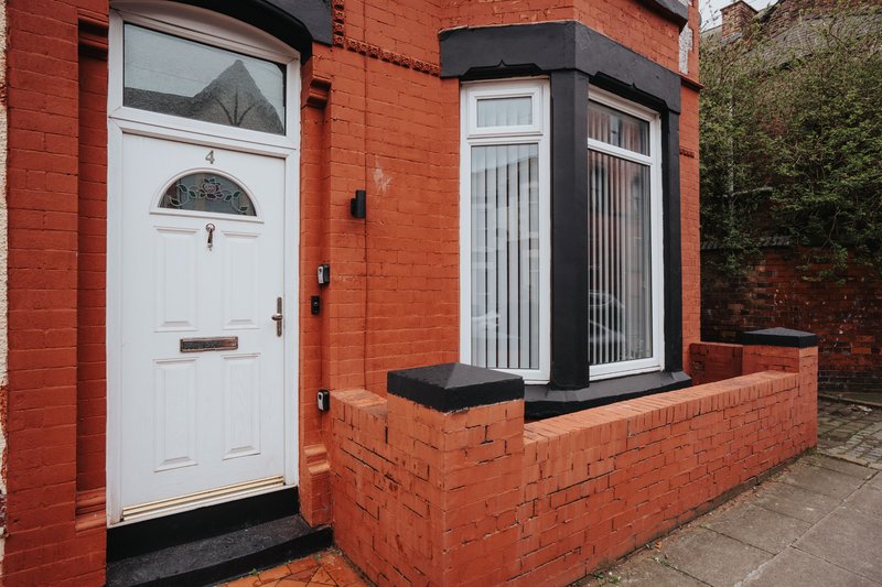 Red brick terraced house exterior with white door, bay window and paved forecourt