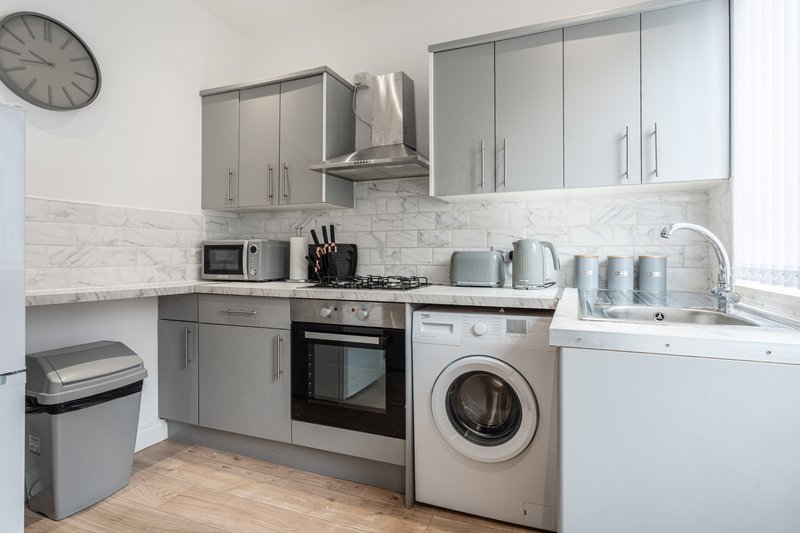 Modern kitchen with grey cabinetry, marble backsplash, integrated appliances and washing machine