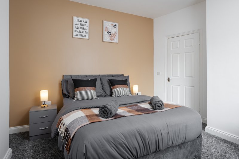 Modern bedroom with grey double bed, peach accent wall, bedside lamps and white door