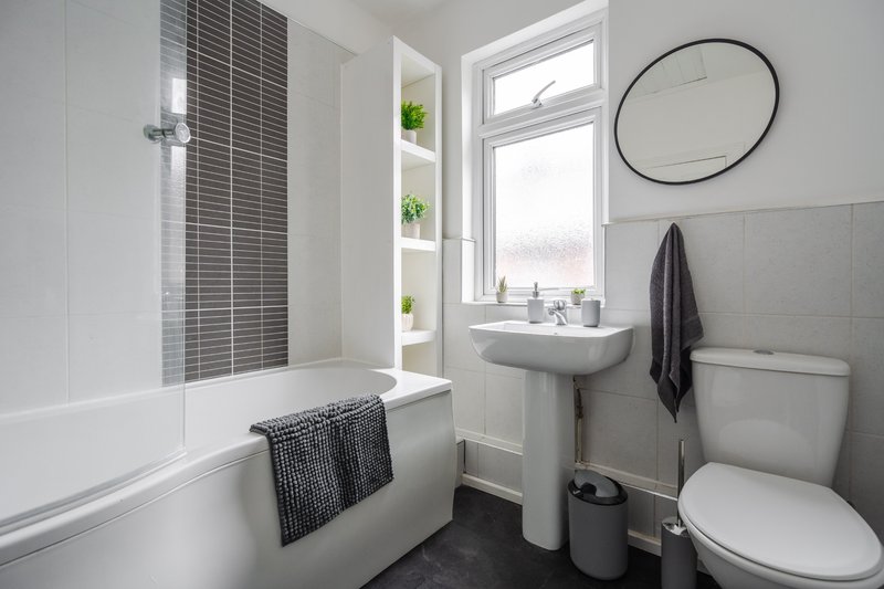 Modern bathroom with bathtub, pedestal sink, toilet, round mirror and window