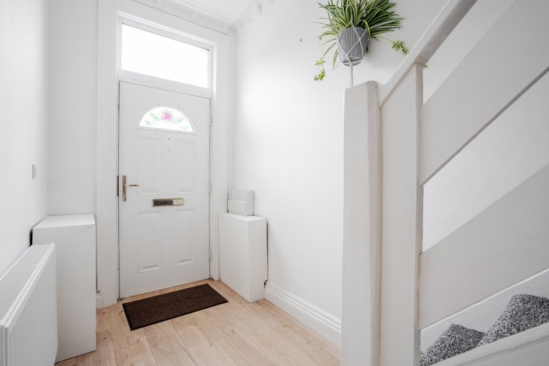Bright entryway with white door, wooden floor, hanging plant and staircase