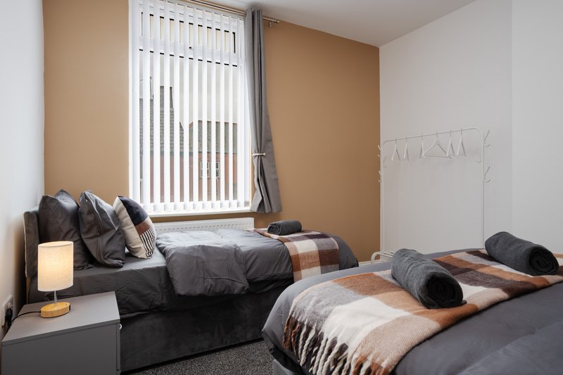 Twin bedroom with dark bedding, beige accent wall, vertical blinds and bedside lamp