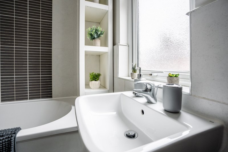 Modern bathroom with white sink, chrome tap, built-in shelving with plants and window