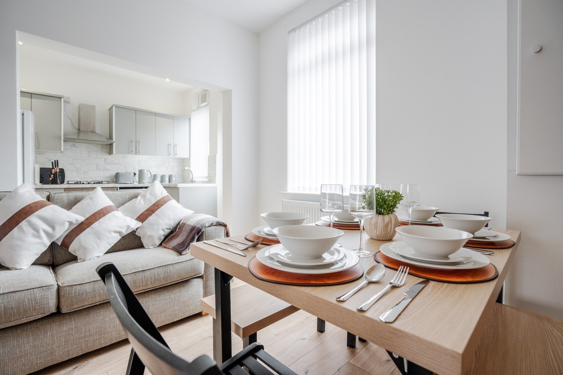 Open-plan living space with dining table, place settings, sofa and kitchenette visible