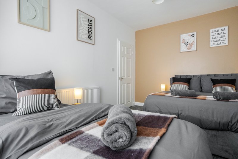 Bright bedroom with two single beds, grey bedding, rolled towel, and peach accent wall