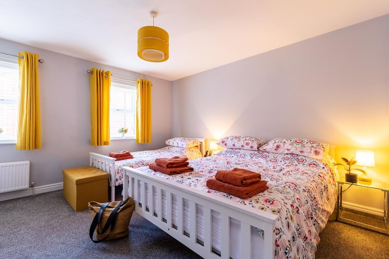 Bright bedroom with double bed, yellow curtains, bedside lamps, and folded towels on bed