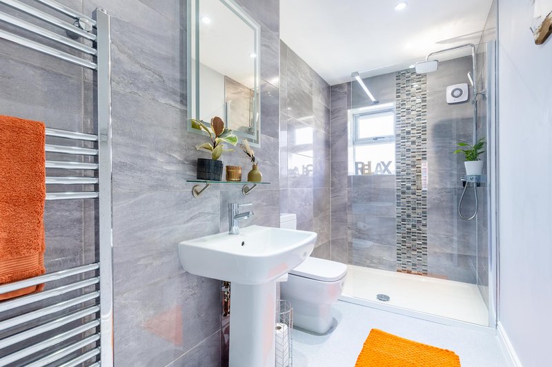 Modern bathroom with pedestal sink, shower enclosure, heated towel rail and grey tile walls
