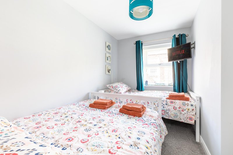 Bright bedroom with double bed, floral bedding, teal curtains and ceiling light