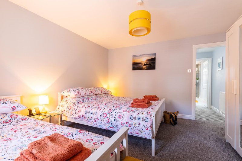 Bedroom with two single beds, pink patterned bedding, yellow ceiling lamp and warm lighting