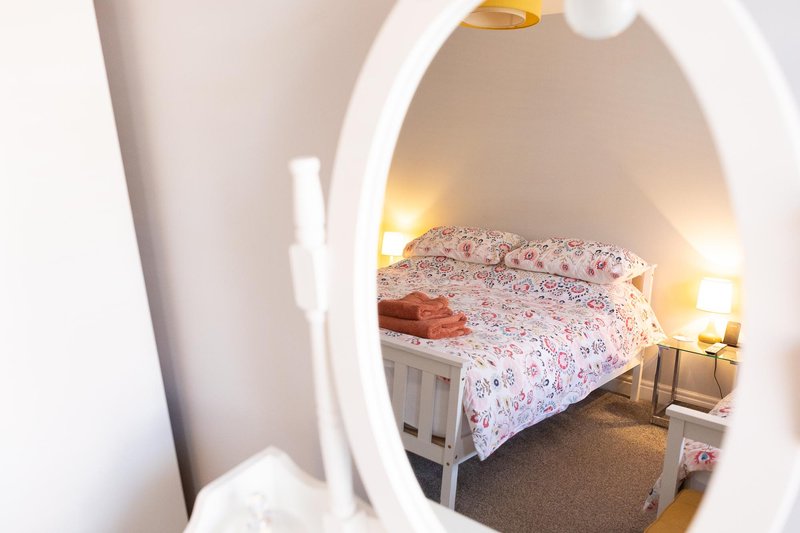 Bedroom with double bed, floral bedding, and warm lamp lighting through doorway