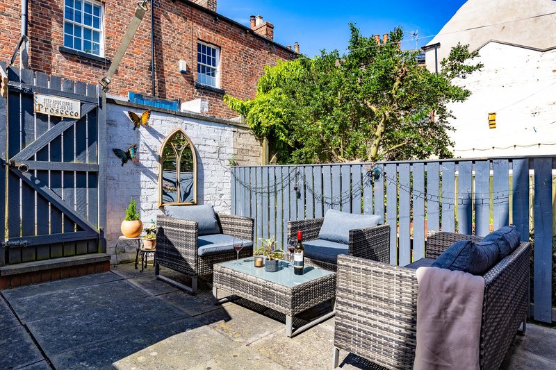 Outdoor patio with wicker furniture, cushions, potted plants and brick building backdrop