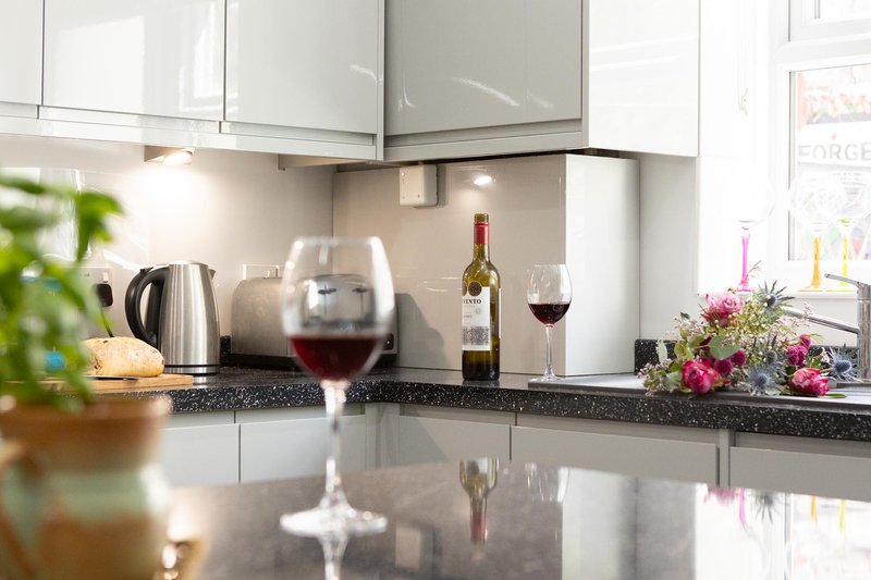 Modern kitchen with white cabinets, dark countertop, wine glasses and bottle, kettle and flowers
