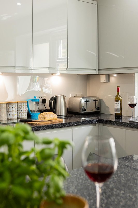 Modern kitchen with white gloss cabinets, granite countertop, kettle, toaster, wine glass and bottle