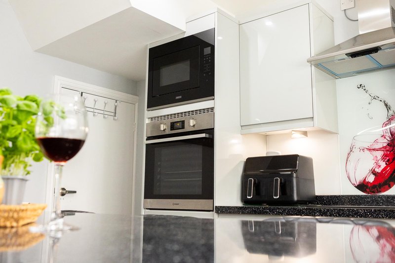 Modern kitchen with built-in microwave and oven, white cabinetry, black countertop, and wine glass on counter