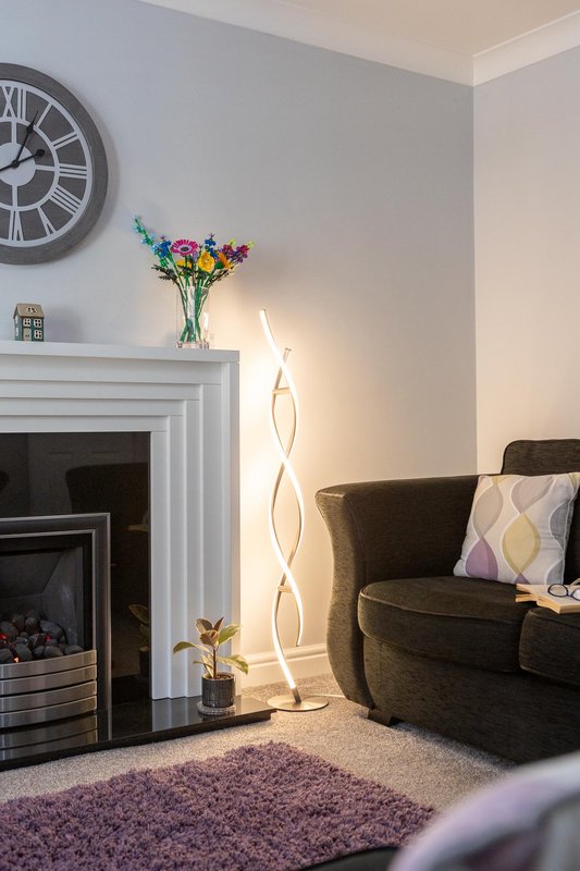 Living room with fireplace, armchair, floor lamp, clock, and colorful flowers in vase
