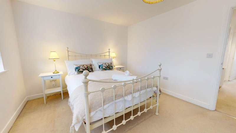 Bright bedroom with metal-frame bed, white bedding, two bedside lamps and wooden flooring