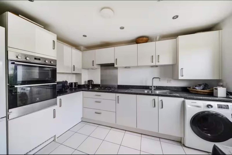 Modern white kitchen with black countertops, integrated appliances and washing machine
