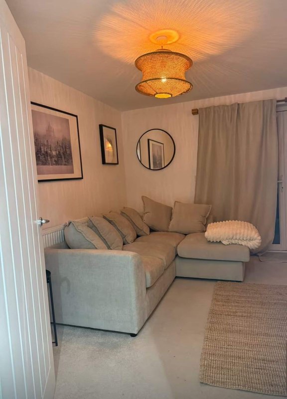 Living room with light gray sofa, decorative cushions, round mirror, framed wall art, and warm ceiling light