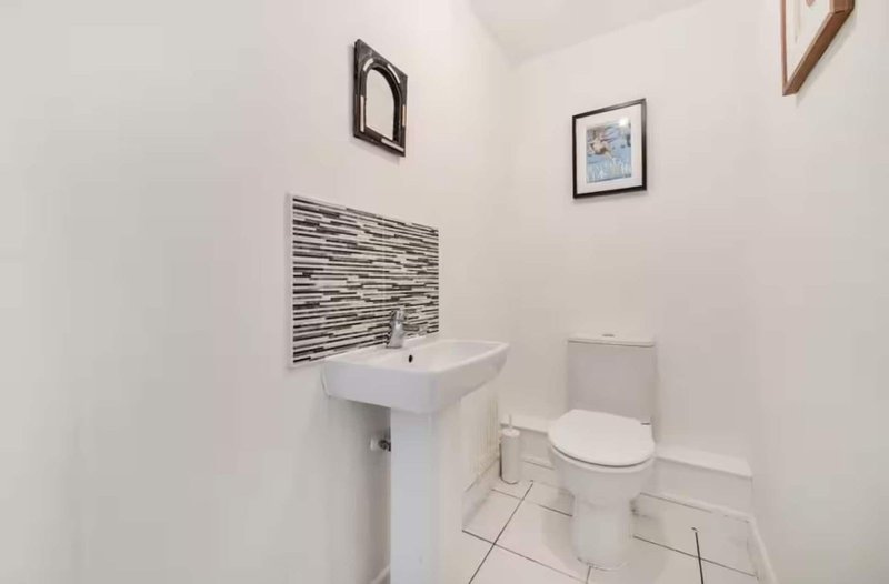 Small white bathroom with pedestal sink, toilet, and tiled floor with wall art