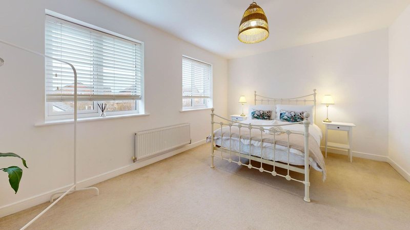 Bright bedroom with metal-frame bed, two windows with blinds, bedside lamps and wooden flooring